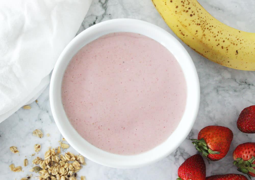 Strawberry smoothie in white bowl surrounded by toppings
