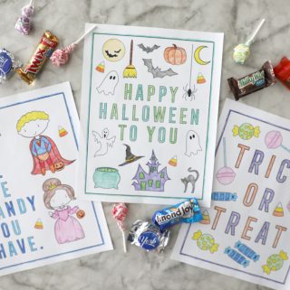 three halloween coloring pages colored in on a marble counter surrounded by candy groupings