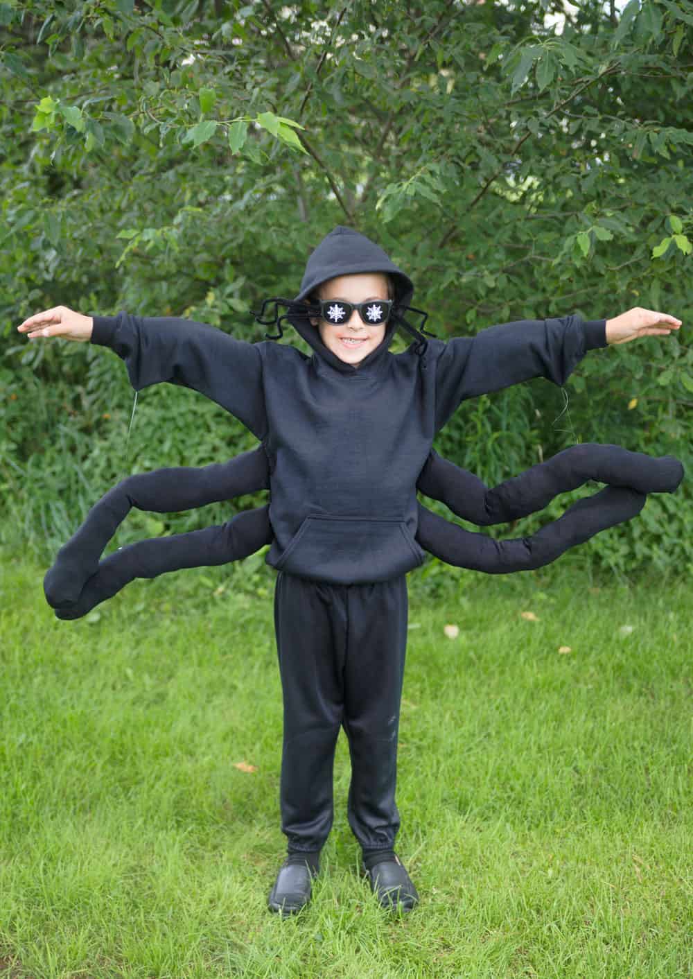 young boy in a spider costume against green grass and green trees
