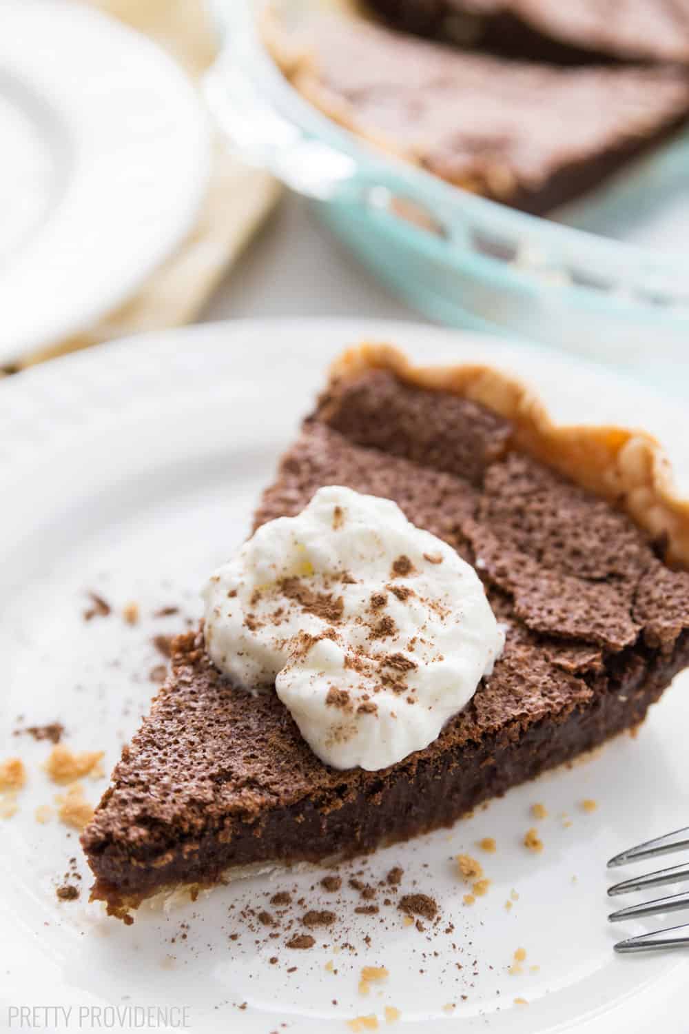 Slice of Chocolate Chess Pie on a white plate, topped with whipped cream and dusted with cocoa powder.