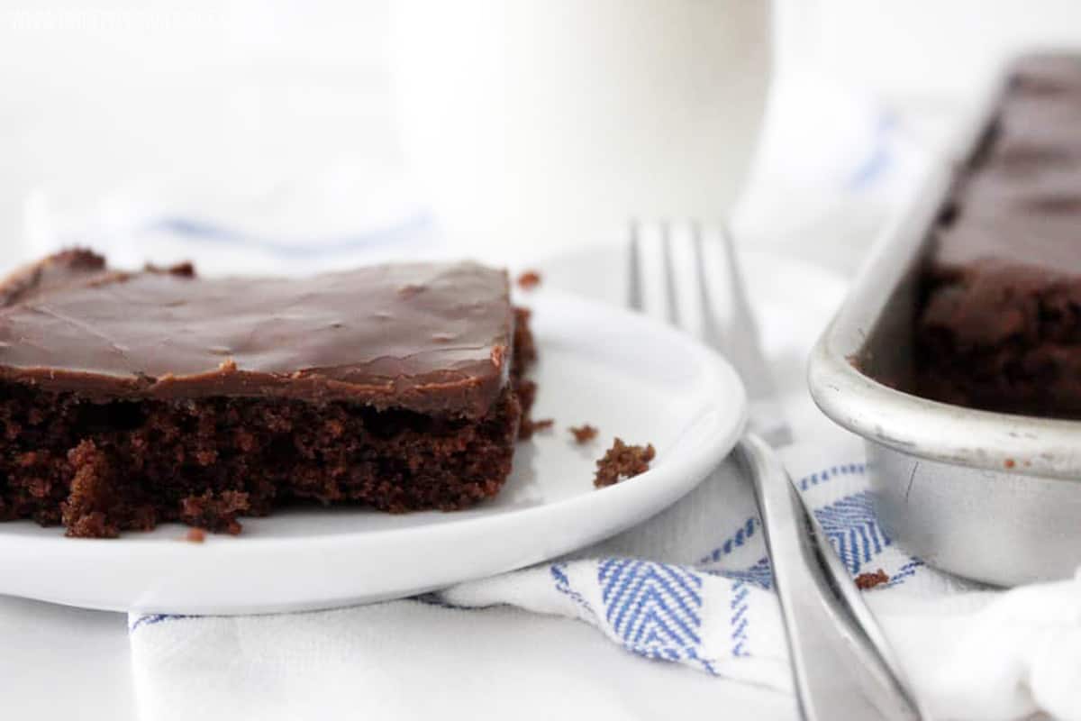 slice of texas sheet cake next to a fork, milk, and the rest of the cake