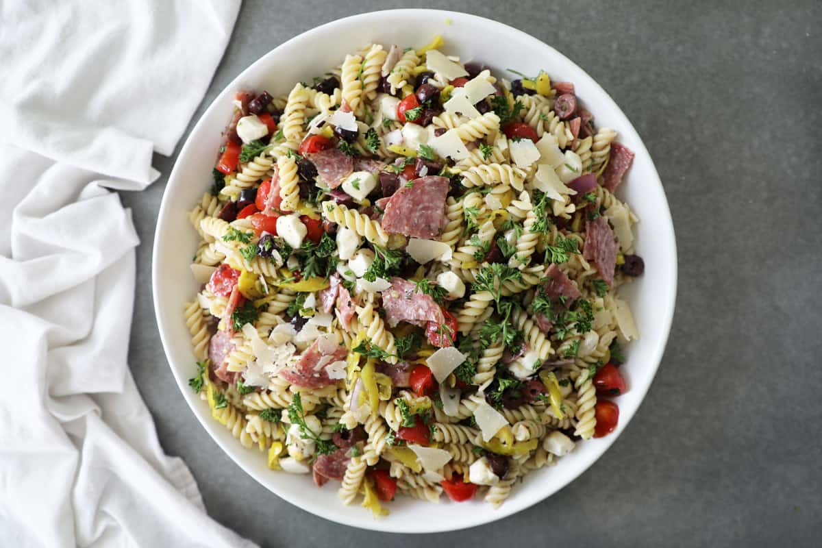 large white bowl of Italian pasta salad on a cement countertop next to a white tea towel