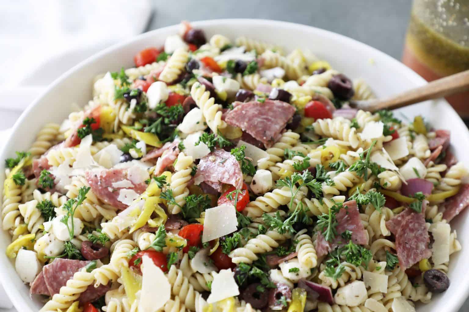 top half of a bowl of pasta salad with a white napkin on the left and salad dressing on the top right