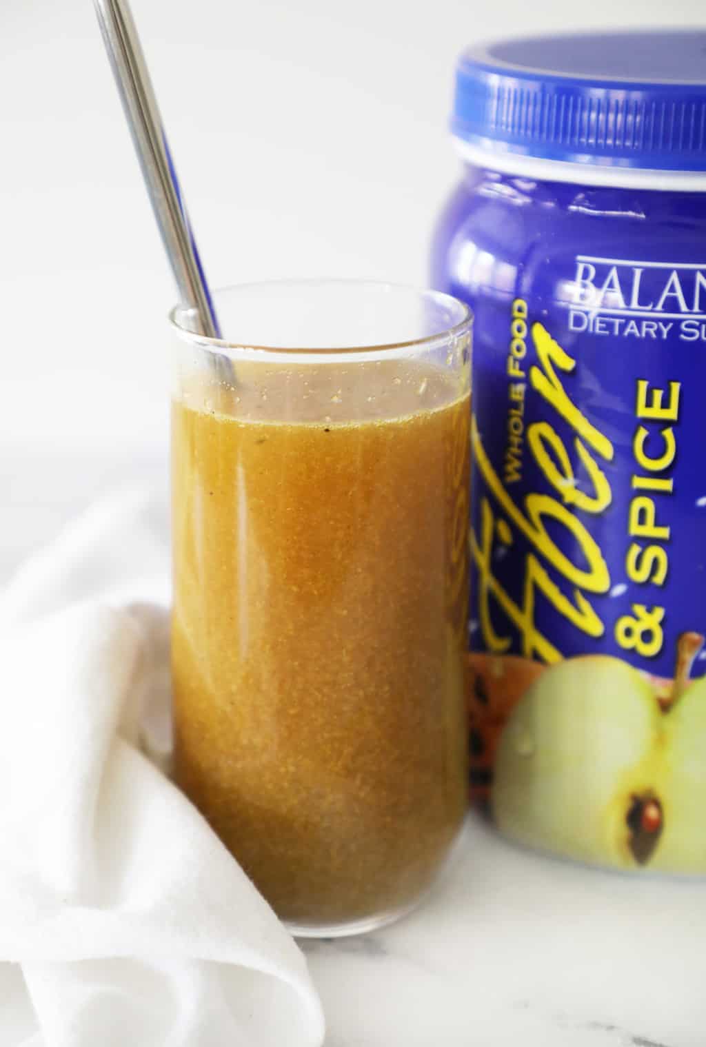 fiber and spice mixed in a clear glass next between the container and a white towel with a spoon sticking out