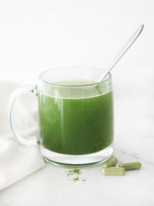 BON veggie capsules diluted in water in a clear mug with a spoon sticking out